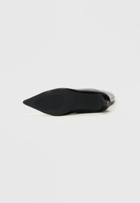 Zapato negro de punta afilada, parte superior de cuero suave, tacón delgado, suela de goma texturizada con surcos horizontales, diseño minimalista, sin adornos.