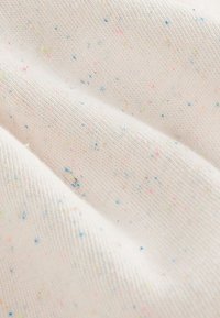 Približni posnetek mehke bele pletene tkanine z majhnimi večbarvnimi pegami v modri, roza, rumeni in zeleni barvi, razpršenimi po celotni površini.