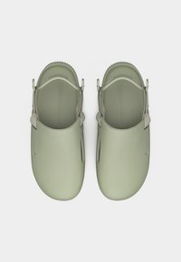 Ζευγάρι ανοιχτόχρωμων πράσινων αφαιρούμενων παπουτσιών με ρυθμιζόμενα λουράκια στη φτέρνα και υφασμένα πέλματα, εμφανιζόμενα από πάνω σε λευκό φόντο.