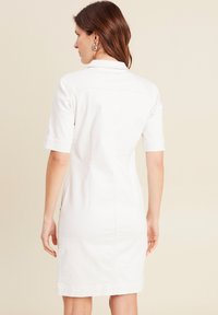 Robe blanche à manches courtes avec un col, design ajusté et une couture le long du dos, fabriquée à partir d'un tissu lisse.