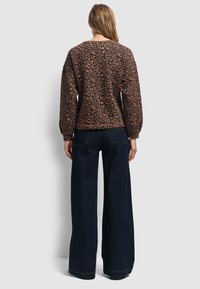 Sweatshirt en imprimé léopard marron avec un col rond et des épaules tombantes, associé à un jean large taille haute bleu foncé.