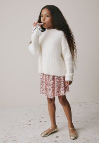 Girl wearing a fluffy white sweater and a pink sequined skirt, holding silver streamers. Gold flat shoes complete the outfit.