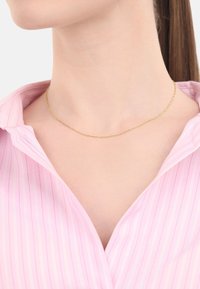 Gouden gedraaide kettinghanger gedragen over een roze gestreepte shirt, met een delicate en minimalistische uitstraling en fijne schakels.
