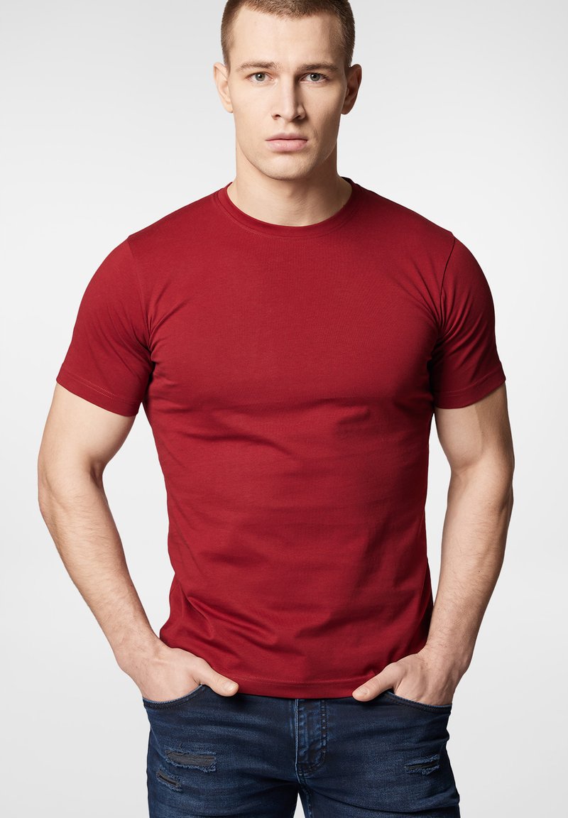 Czerwona bawełniana koszulka z krótkim rękawem i okrągłym dekoltem, gładka w dotyku, dopasowana, noszona z niebieskimi dżinsami z przetarciami.