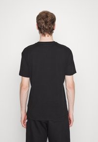 T-shirt noir à manches courtes en coton, avec une coupe décontractée, un col rond et des coutures épurées, présenté de dos.