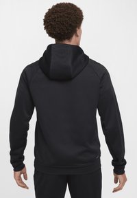 Zwarte hoodie met een gestructureerd ontwerp, lange mouwen en een ontspannen pasvorm. Heeft een kangoeroezak. Glad materiaal.