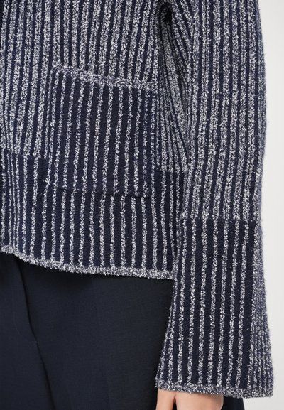 Tmavomodrý sveter so svetlými vertikálnymi pruhmi, štruktúrovanou látkou, širokými rukávmi a voľným strihom, doplnený predným vreckom.