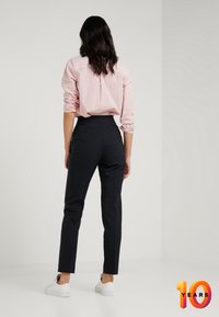 Tmavě modré kalhoty na míru v kombinaci s červenou a bílou pruhovanou košilí, s vysokým pasem a slim fit. Bílé tenisky celé look doplňují.