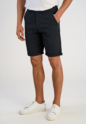 Pantaloni corti neri in cotone con orli risvoltabili, tasche laterali e un design frontale piatto, abbinati a sneakers bianche.