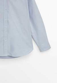 Chemise bleu clair à manches longues avec boutons visibles, bord de col et ourlet sur fond blanc.
