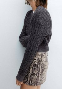 Grå strikket sweater med lange ærmer og et struktureret mønster, parret med en tætsiddende nederdel i slangeskindsmønster i nuancer af beige og brun.