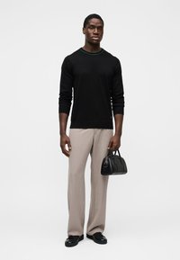 Schwarzer Pullover mit langen Ärmeln und türkisfarbenem Kragen, beigefarbene, weit geschnittene Hosen und eine kleine schwarze Handtasche, ergänzt durch schwarze Schuhe.