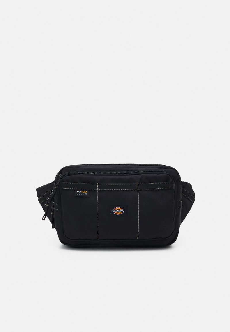 Sac à bandoulière en tissu noir avec des coutures jaunes contrastantes, dotée d'une fermeture éclair et de patchs de logo sur le devant.