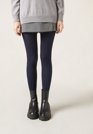 Navy leggings i mjukt tyg, matchade med en grå tröja och en lager-på-lager kjol, bärs tillsammans med svarta läderstövletter.