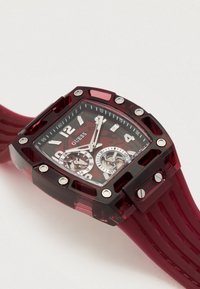 Kvadratisk rød ur med gennemsigtig kasse, metalliske accenter, dobbelte kronograf-skiver og en tekstureret silikonerem.