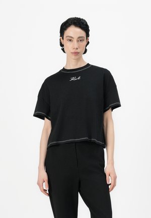 T-shirt noir court à manches courtes, avec des coutures contrastées et un logo brodé subtil près du col. Tissu en coton doux.