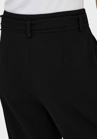 Pantaloni neri su misura con vita alta e passanti per cintura indossati con una maglia bianca a costine.