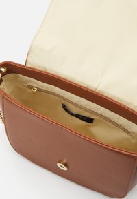 Borsa a tracolla in pelle marrone con patta aperta, interno in tessuto beige, tasca con zip interna e chiusura magnetica dorata.