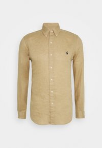 Hnědá košile s dlouhým rukávem, s knoflíkovým límečkem a malým tmavým logem na levé hrudi na bílém pozadí.