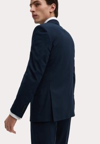 Donkerblauwe colbert gemaakt van gladde stof, met een enkele split, details van acht knopen op de mouwen en witte shirtmanchetten die eronderuit steken.