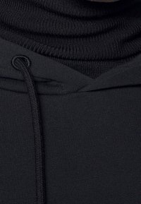 Czarna bluza z kapturem z wysokim kołnierzem o ryftowanej fakturze oraz przednia kieszeń typu kangur. Sznurek jest widoczny przy dekolcie.