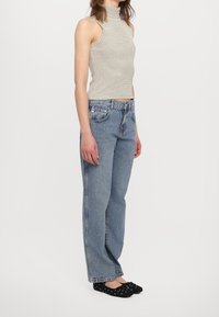 Top smanicato a righe con collo alto, jeans in denim a gamba dritta e ballerine nere con pois bianchi, indossati in una posa in piedi.