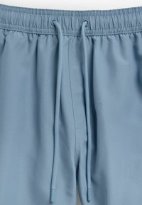Pantaloni de trening de un albastru deschis, cu un tiv elastic, șnururi ajustabile, textură netedă a țesăturii și detalii de cusătură subtile.
