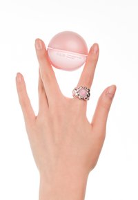 Contenant sphérique rose pour masque à lèvres, étiqueté "Abib", tenu par une main portant une bague argentée en forme de fleur avec un détail en pierre rose.