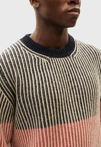 Knit sweater featuring vertical black and cream stripes with a pink section at the bottom. Round navy collar and textured fabric.