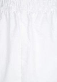 Tessuto bianco con una texture liscia, dotato di una cintura elastica e design senza cuciture, adatto per abbigliamento casual o sportivo.