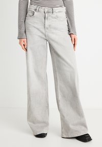 Ανοιχτό γκρι, τζιν παντελόνι με ψηλή μέση και φαρδύ πόδι με ελαφρώς ξεθωριασμένη εμφάνιση, διαθέτει μπροστινές τσέπες και θηλιές για ζώνη. Το ύφασμα είναι απαλό τζιν με χαρακτηριστικό ράψιμο.