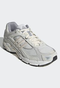 Világosszürke sportcipő hálós panelekkel, három oldalsó csíkkal, texturált díszítésekkel és párnázott talppal. Kerek orrú és fűzős.