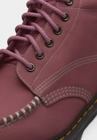 Κοντινό πλάνο μποτάκι από δέρμα σε μωβ απόχρωση με ροζ κορδόνια, λευκή ραφή, μεταλλικές τρύπες και μαύρη σόλα με κίτρινη ραφή.