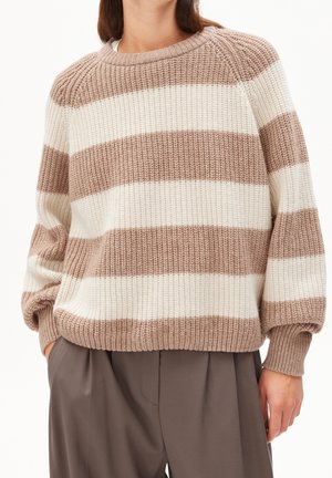 Neulepusero, jossa leveät beigevalkoiset vaakaraitakuviot, laskostetut olkapäät ja pitkät ilmapallohihat, yhdistettynä löysiin ruskeisiin housuihin.