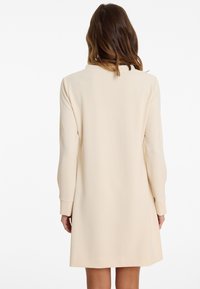 Cremefarbenes Kleid aus glattem Stoff, mit langen Ärmeln und einer lässigen, geraden Silhouette, Rundhalsausschnitt und ohne sichtbare Muster.