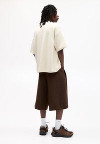 Beżowy oversize t-shirt, brązowe szorty do kolan, czarne i brązowe sneakersy oraz białe skarpetki. Prosty, luźny design z minimalistycznymi cechami.