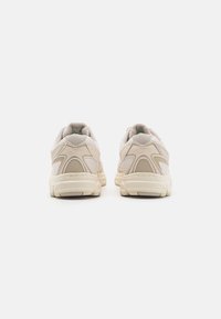 Beige Sport Schuhe mit Mesh-Obermaterial, strukturierten Akzenten und gepolstertem Kragen. Verfügt über eine dicke Sohle mit sichtbarem Grip-Muster.