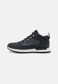 Navy blue hiking shoe with suede and textile upper, white midsole, black outsole, and metallic eyelets. Features a rear pull tab for easy wear.
