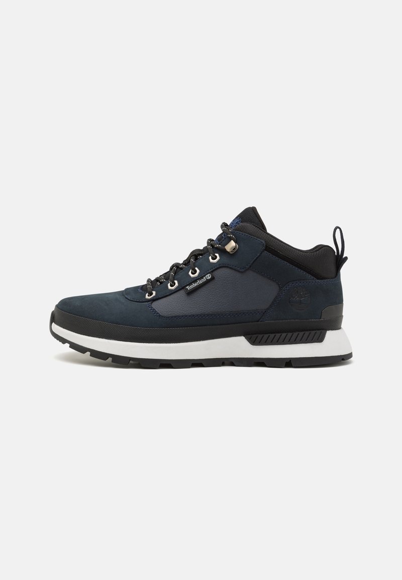 Navy blue hiking shoe with suede and textile upper, white midsole, black outsole, and metallic eyelets. Features a rear pull tab for easy wear.