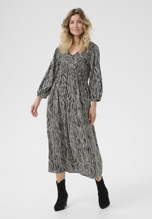 Lang zwart-wit gestreept jurk met pofmouwen, een V-hals en een cinched taille, gecombineerd met zwarte enkellaarzen.