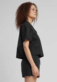 Top nero corto con maniche corte e tessuto testurizzato, abbinato a pantaloni corti neri coordinati con coulisse.
