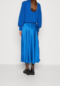 Sininen neulottu lyhyt villapaita puffi hihoilla, yhdistettynä satiiniseen siniseen midihameeseen. Mustat paksupohjaiset kengät viimeistelevät asun.