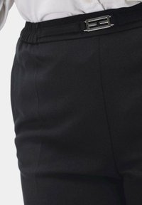Zwarte broek met een gladde textuur, elastische tailleband en een zilveren gesp met een geometrisch ontwerp om te sluiten.