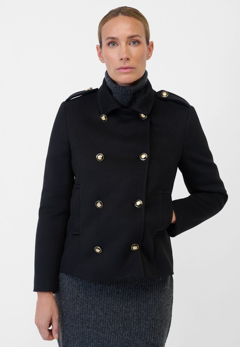 Black double-breasted coat made of textured fabric with gold buttons, featuring a mandarin collar and side pockets, paired with a gray knit dress.