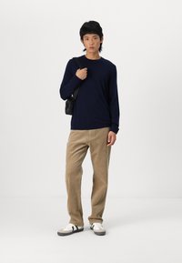Dunkelblaues Langarmhemd, beige Cordhosen und weiße Sneaker mit schwarzen Akzenten. Kleine schwarze Umhängetasche. Schlichtes, lässiges Design.
