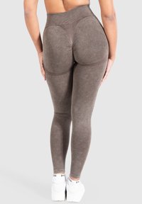 Leggings marroni a vita alta con una texture liscia e un design del retro accentuato. Presentano un cinturino a coste e sono indossati con scarpe da ginnastica bianche.