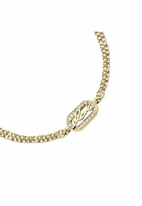 Guld kedja armband med ett rektangulärt spänne prytt med klara kristaller och ordet "Karl" i kursiv. Kedjelänkarna har textur.