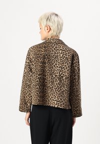 Jas met luipaardprint van een zachte textuur, lange mouwen en een kraag. Het ontwerp is boxy met een cropped zoom, gecombineerd met zwarte broeken.