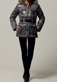 Parka grigia imbottita con cappuccio foderato in pelliccia, chiusura con zip e quattro tasche frontali. Presenta una cintura in vita e una texture trapuntata.