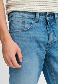 Jeans de mezclilla azul claro con un diseño clásico de cinco bolsillos, un ligero desvanecimiento y una cinturilla estándar con cierre de botón.